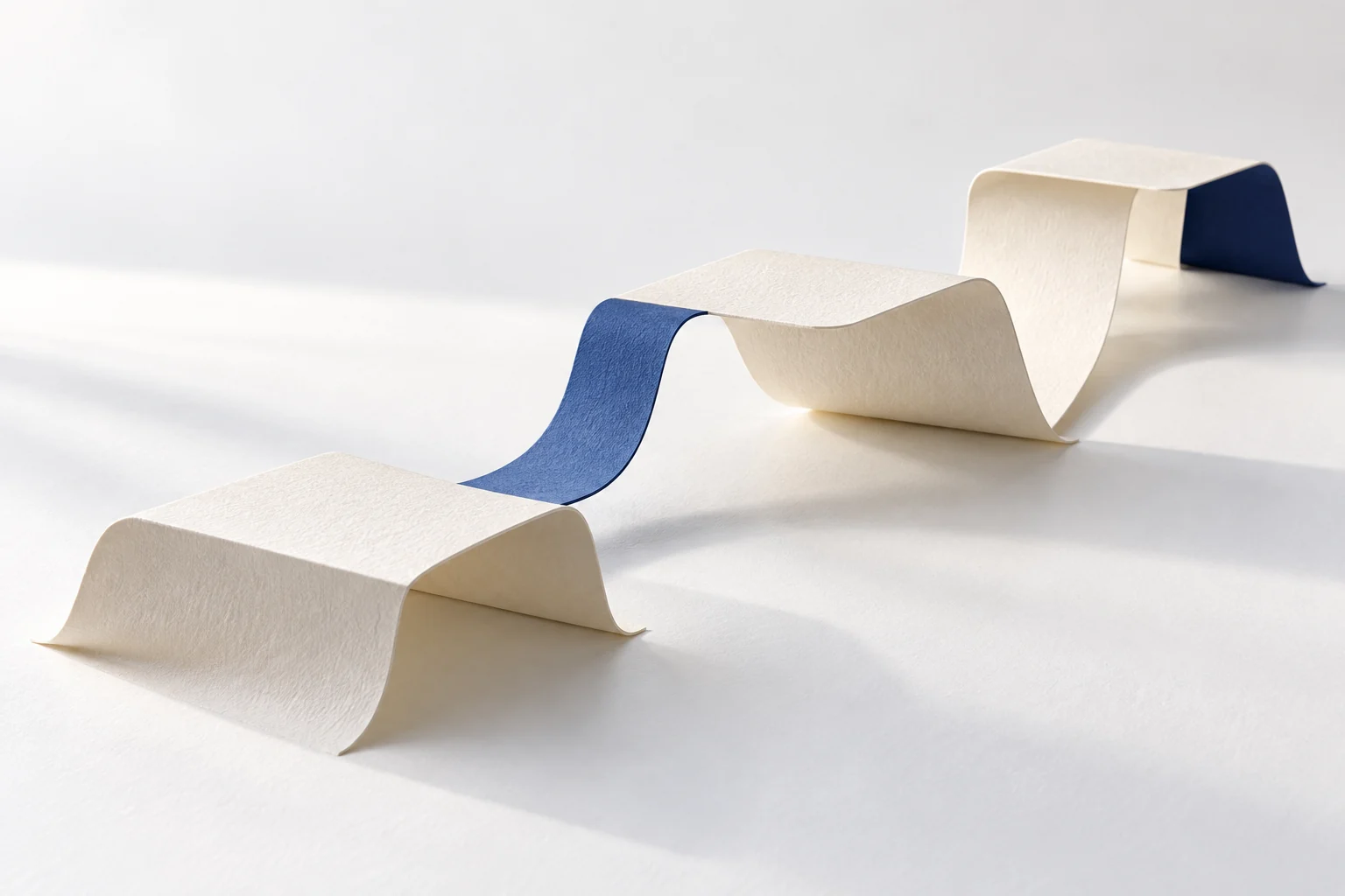 Eine gefaltete Papierbahn mit blauen Abschnitten verläuft über einen weißen Tisch.