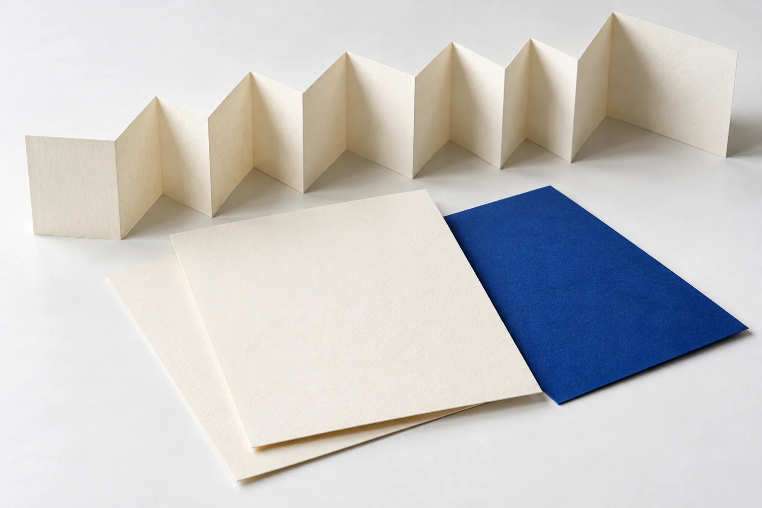 Eine lange gefaltete Papierbahn liegt neben zwei flachen Papierblättern.