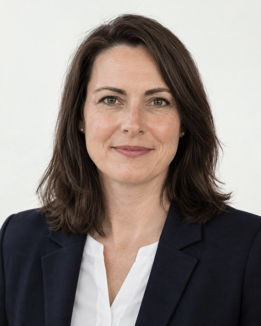 Bewerbungsfoto einer Frau um vierzig in dunkelblauem Blazer und weißer Bluse vor einem hellen, gleichmäßigen Hintergrund, Blick in die Kamera