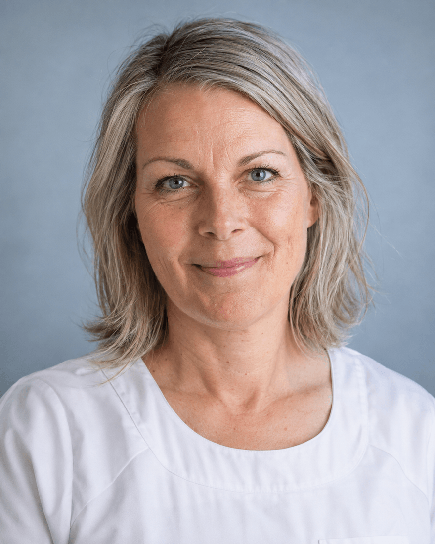 Bewerbungsfoto einer Frau um fünfundvierzig mit schulterlangen graublonden Haaren in weißem Kasack vor hellem blaugrauem Hintergrund, warmer Blick in die Kamera
