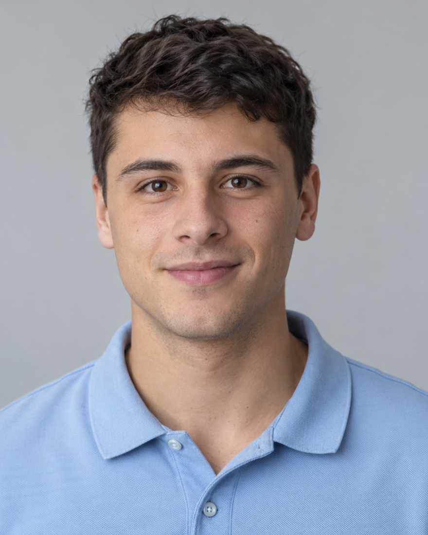 Junger Mann um die zwanzig mit kurzem dunklem Haar und hellblauem Poloshirt vor einer schlichten hellgrauen Wand, freundlicher ruhiger Blick