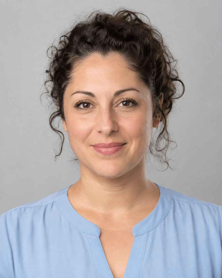 Bewerbungsfoto einer Frau Mitte dreißig mit zurückgebundenen dunklen Locken in hellblauer Bluse vor hellgrauem Hintergrund, ruhiger offener Blick