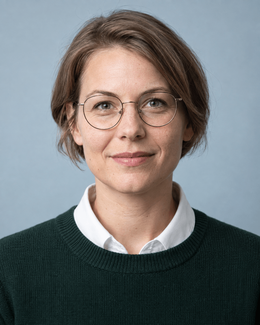 Bewerbungsfoto einer Frau Anfang dreißig mit runder Brille in dunkelgrünem Pullover über weißem Kragen vor blaugrauem Hintergrund, Register Labor und Diagnostik