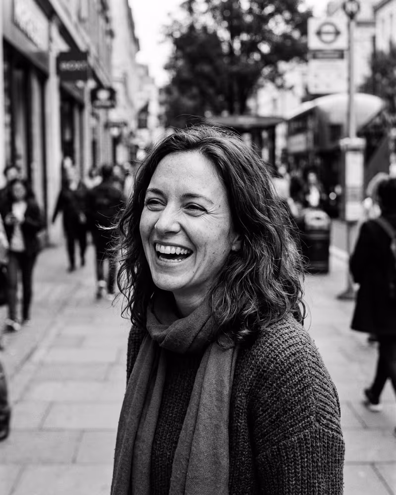 Schwarz-Weiß-Profilbild im Street-Stil: spontanes Lachen vor unscharfer Stadtkulisse