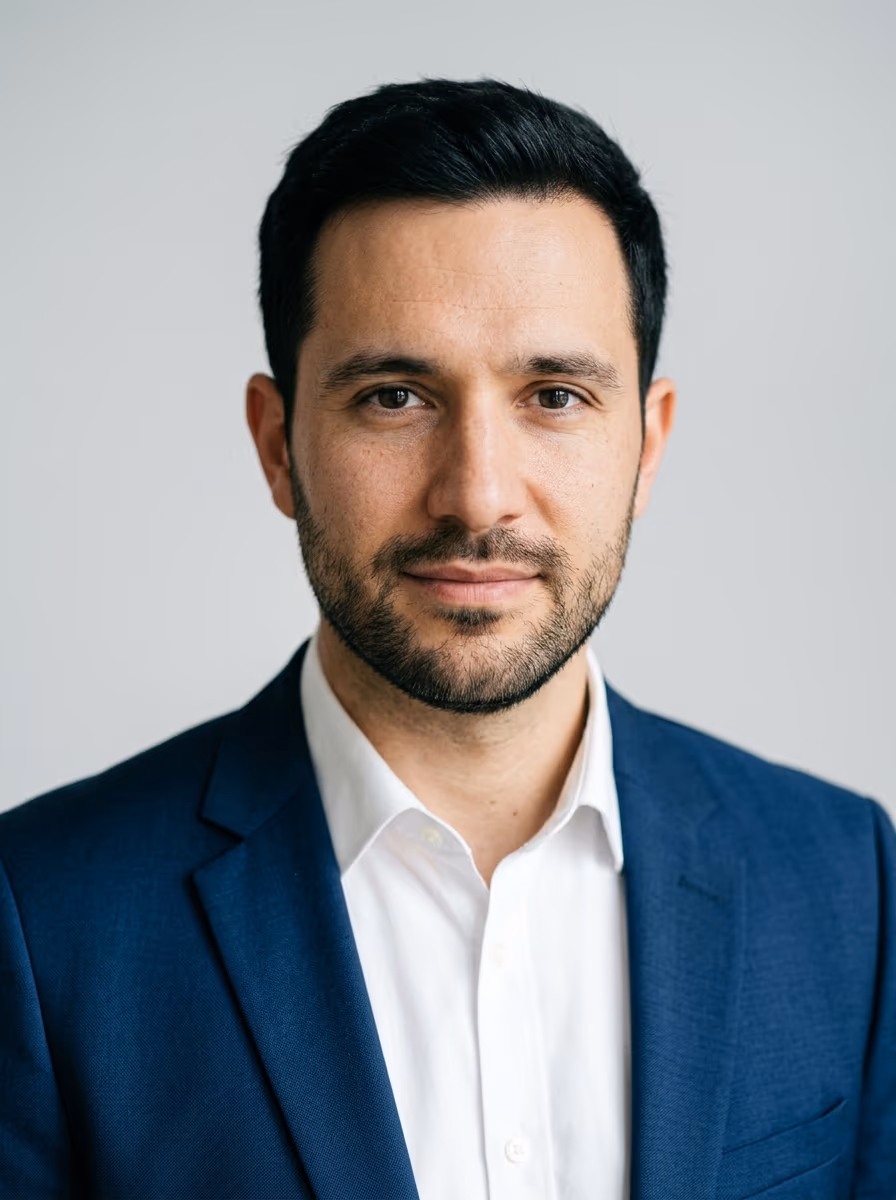 Retrato de um homem de blazer azul e camisa branca diante de fundo cinza-claro, enquadrado dos ombros para cima