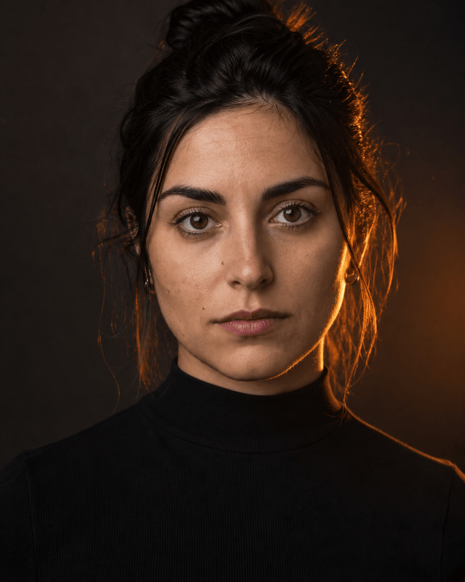 Frau vor dunklem Hintergrund, ein warmes oranges Licht hinter ihrer Schulter zeichnet eine helle Kante an Haar und Wange