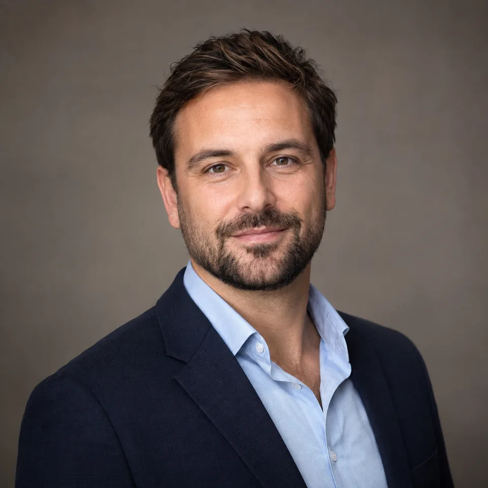 Professional headshot of a man with a neat beard, navy blazer and open-collar blue shirt