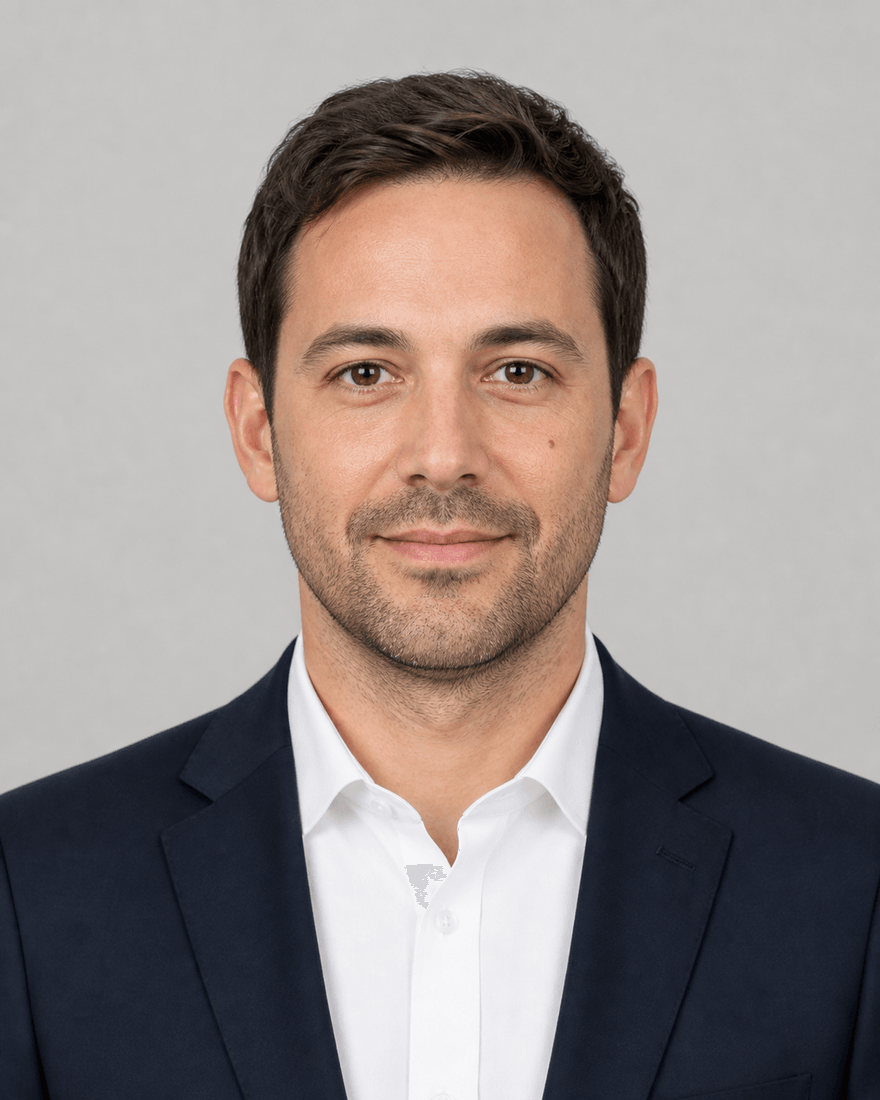Derselbe Mann in einem sehr gleichmäßig ausgeleuchteten Business-Porträt vor glattem
            hellgrauem Hintergrund, frontal, dunkelblaues Sakko über weißem Hemd