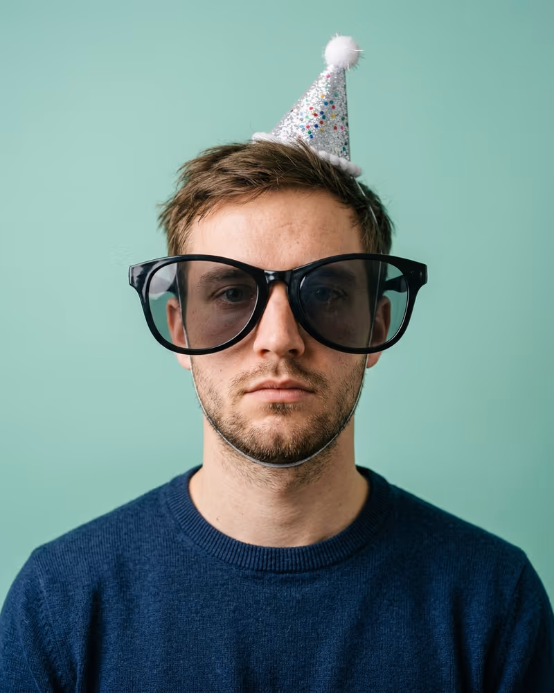 Lustiges Profilbild mit Requisite: Mann mit riesiger Scherzbrille und Mini-Partyhut bei ernstem Blick