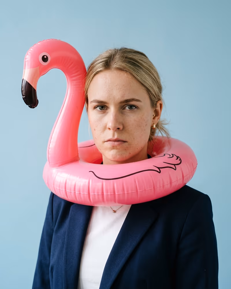 Witziges Profilbild: Frau im Blazer mit pinkem Flamingo-Schwimmring um die Schultern und Business-Miene