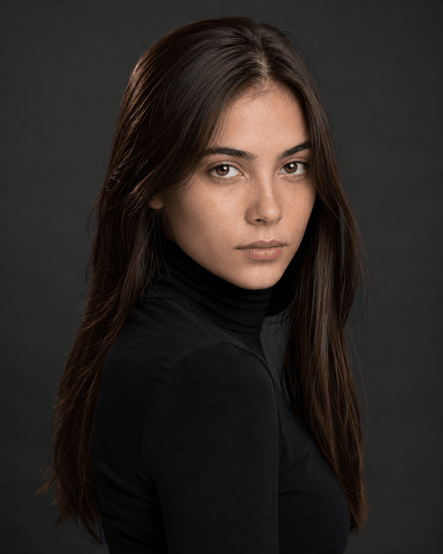 Junge Frau als ausgeleuchtetes Casting-Portrait vor dunkelgrauem Hintergrund, leicht gedrehte Schulter, direkter Blick