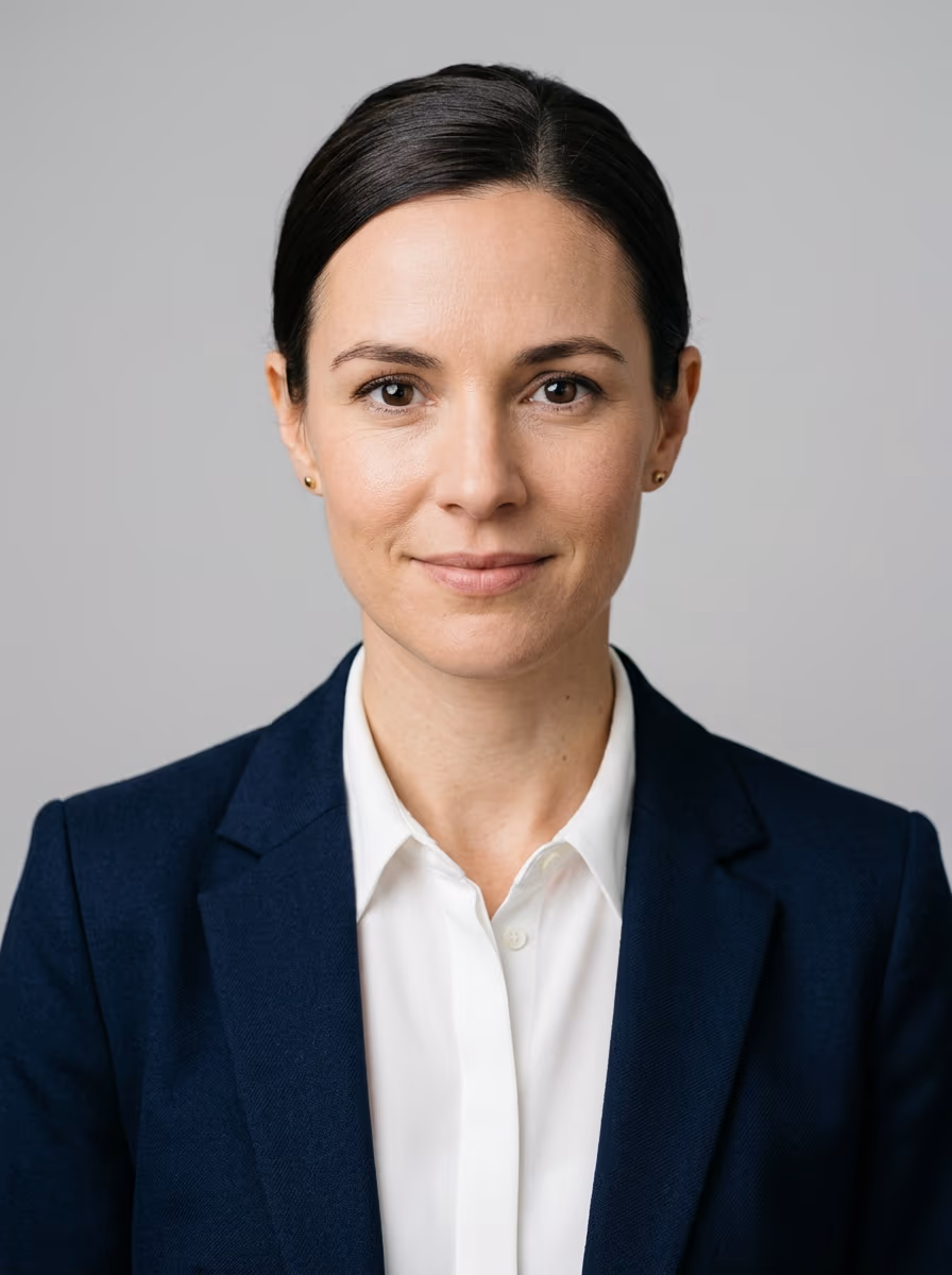 Neutral portrait of a woman in a navy blazer and white shirt against a plain grey background